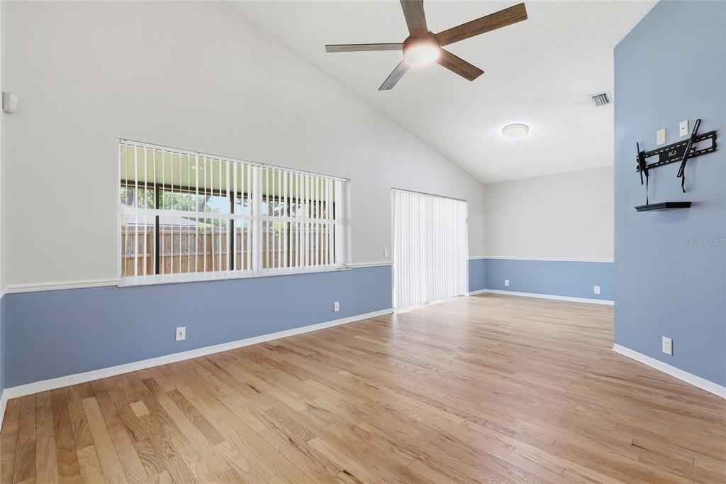 A living room features light blue wainscoting, hardwood floors, a vaulted ceiling, and a ceiling fan — 5724 ERHARDT DRIVE, RIVERVIEW, FL