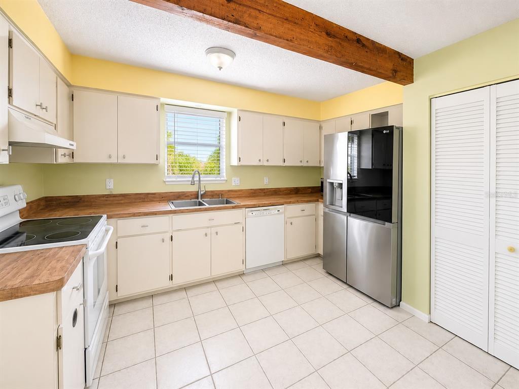 A kitchen features light-colored cabinets, wood-look countertops, a stainless steel refrigerator, and a ceiling beam — 60 BEACHCOMBER LANE UNIT B, ENGLEWOOD, FL