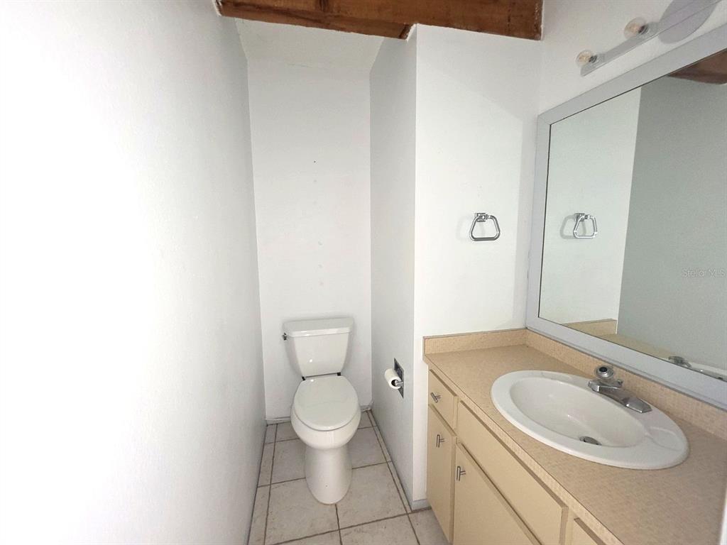 A bathroom features a white toilet, a beige vanity with a sink, and a large mirror — 60 BEACHCOMBER LANE UNIT B, ENGLEWOOD, FL