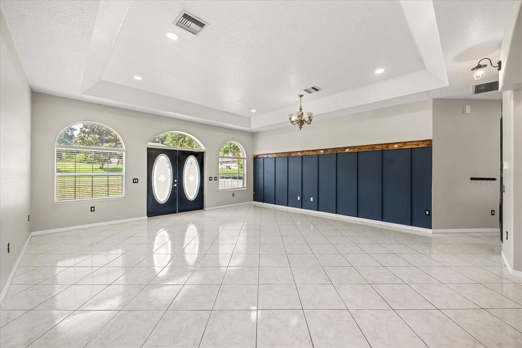 A spacious living room features white tile floors, a tray ceiling, and a dark blue wall — 13848 VISTA DEL LAGO BOULEVARD, CLERMONT, FL