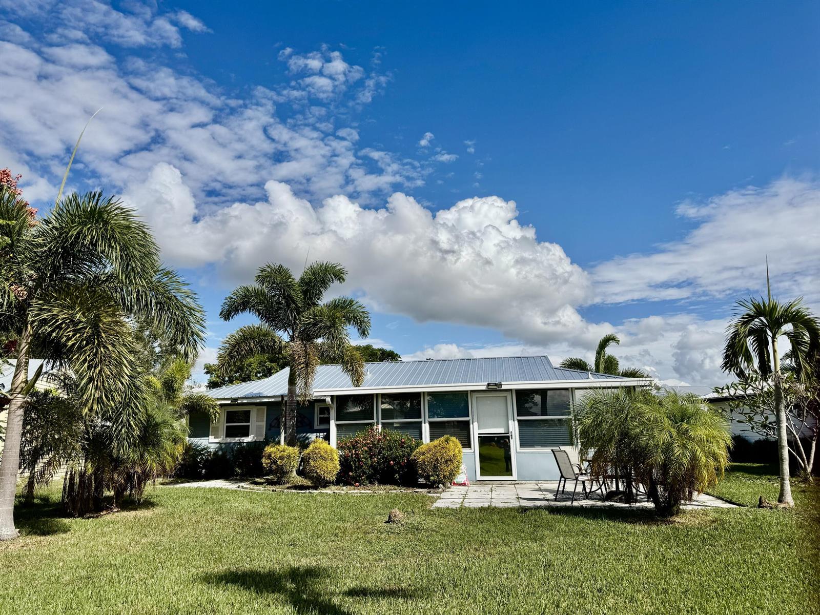A single-story house with a metal roof and palm trees sits on a grassy lawn — 5248 SE 43rd Trace, Okeechobee FL 34974, OKEECHOBEE, FL