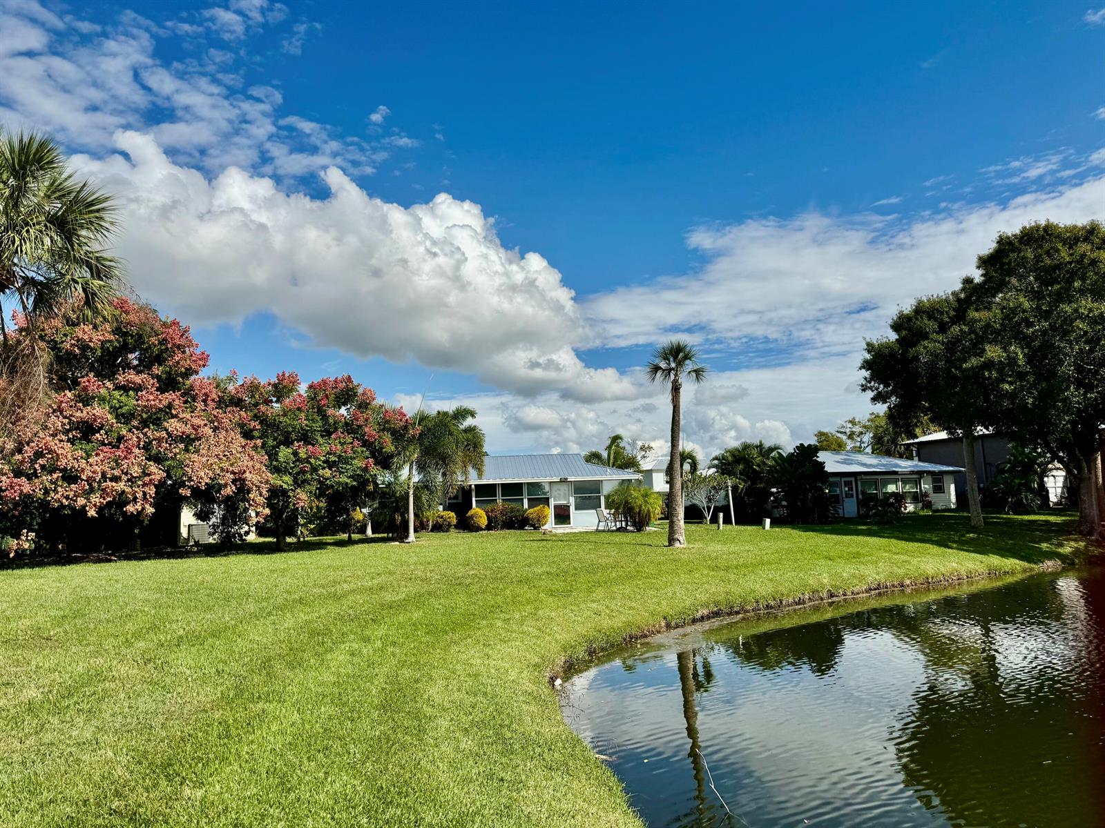 A grassy lawn leads to a house with a blue roof beside a small pond — 5248 SE 43rd Trace, Okeechobee FL 34974, OKEECHOBEE, FL
