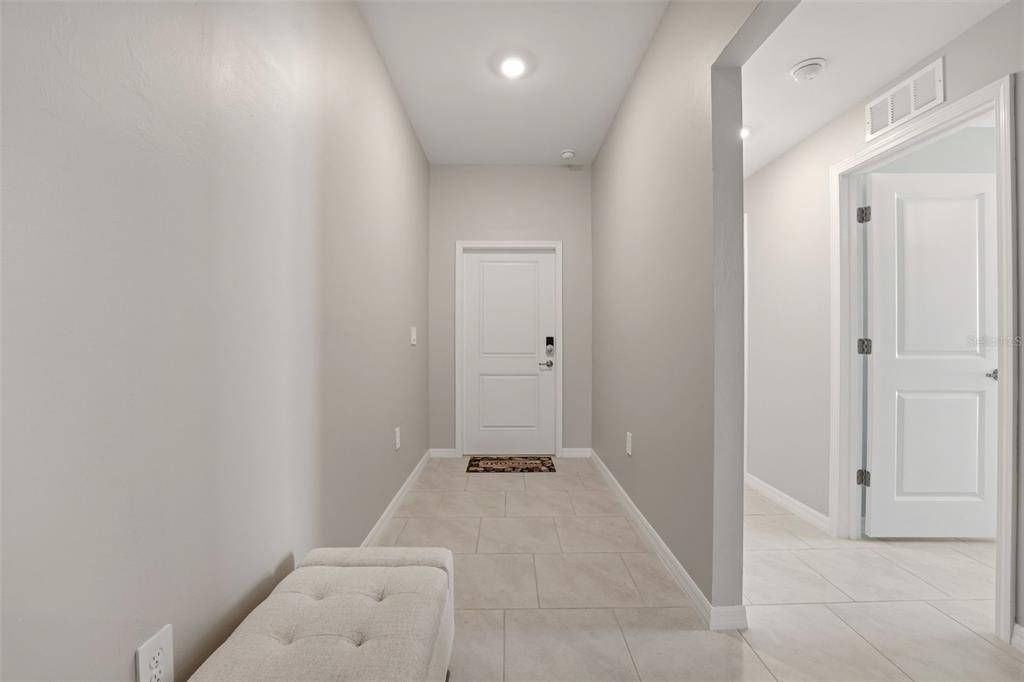 A tiled entryway features a white front door, a light gray bench, and neutral walls — 113 LEISURE PLACE, ROTONDA WEST, FL