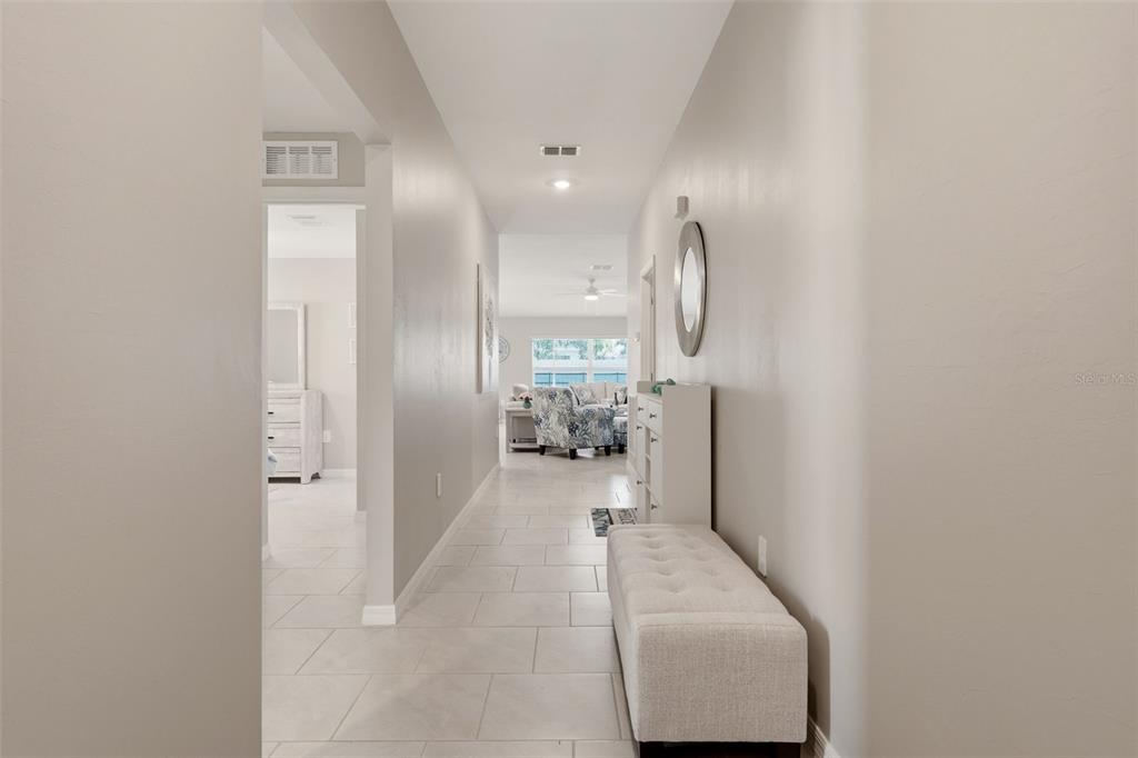 A hallway with light tile flooring leads toward a living area with a patterned chair — 113 LEISURE PLACE, ROTONDA WEST, FL