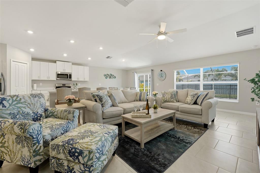 A bright living room features light-colored furniture, a patterned armchair, and tile flooring — 113 LEISURE PLACE, ROTONDA WEST, FL