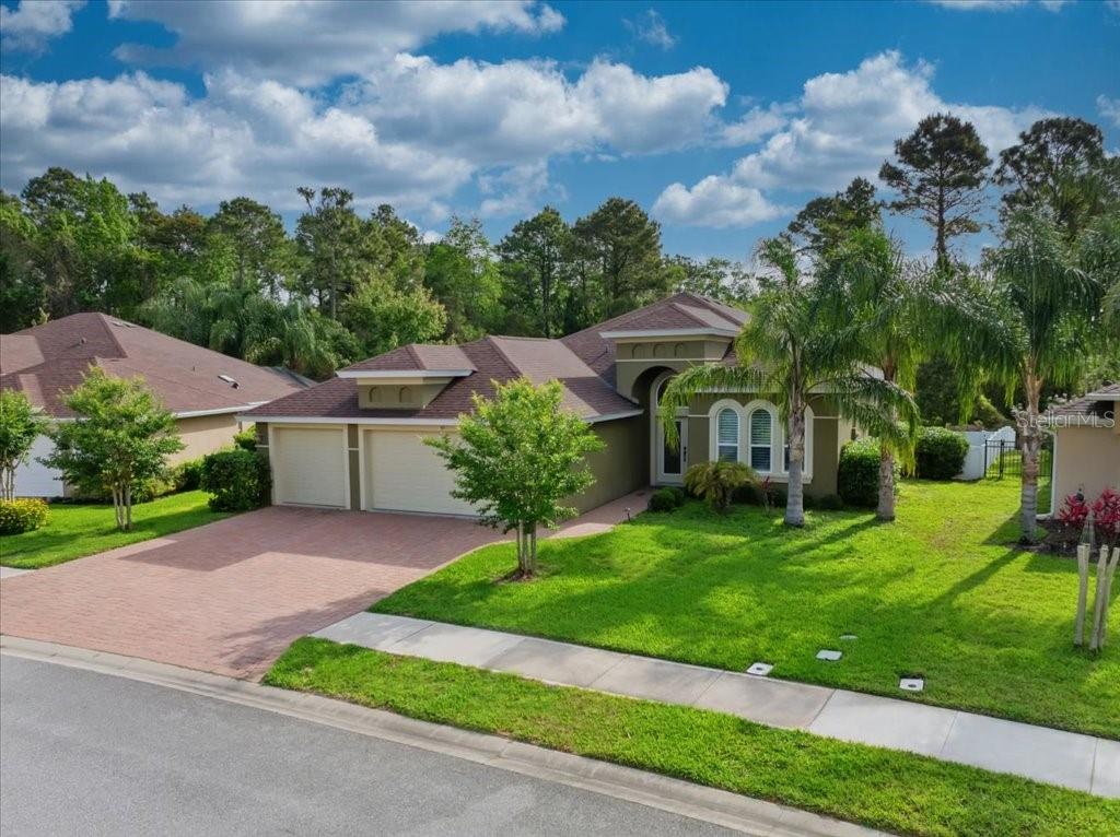 A single-story house with a two-car garage, brick driveway, and palm trees in the front yard — 45 GRAHAM WOODS PLACE, PALM COAST, FL