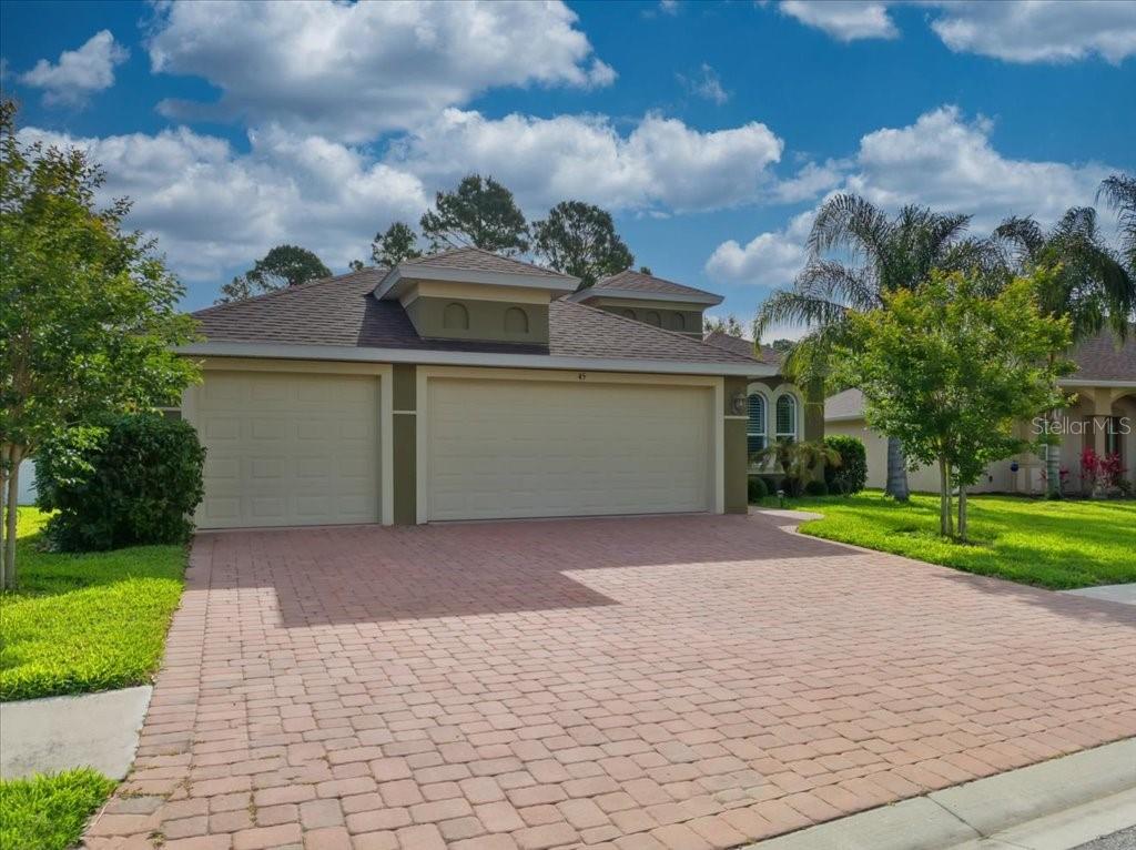 A single-story house with a three-car garage and a paved driveway under a cloudy sky — 45 GRAHAM WOODS PLACE, PALM COAST, FL