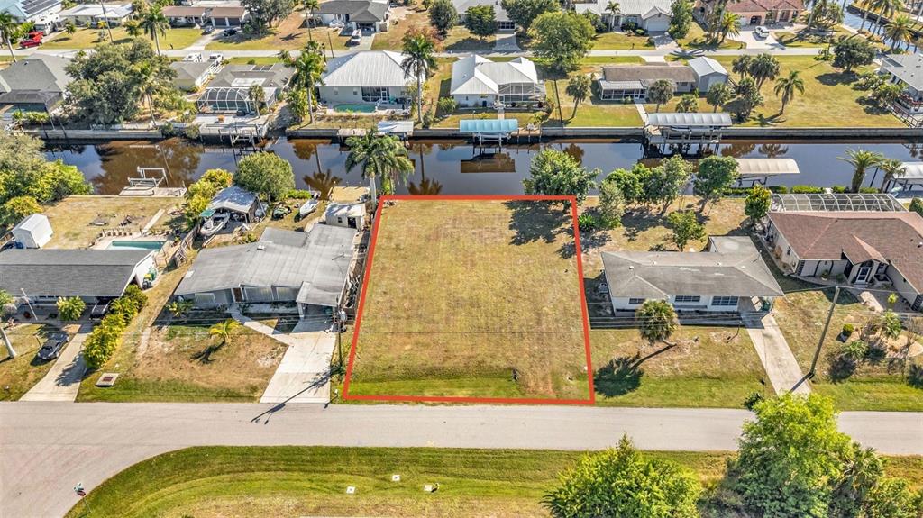 An aerial view shows a vacant rectangular lot situated between two houses along a canal — 3334 DOVER DRIVE, PUNTA GORDA, FL