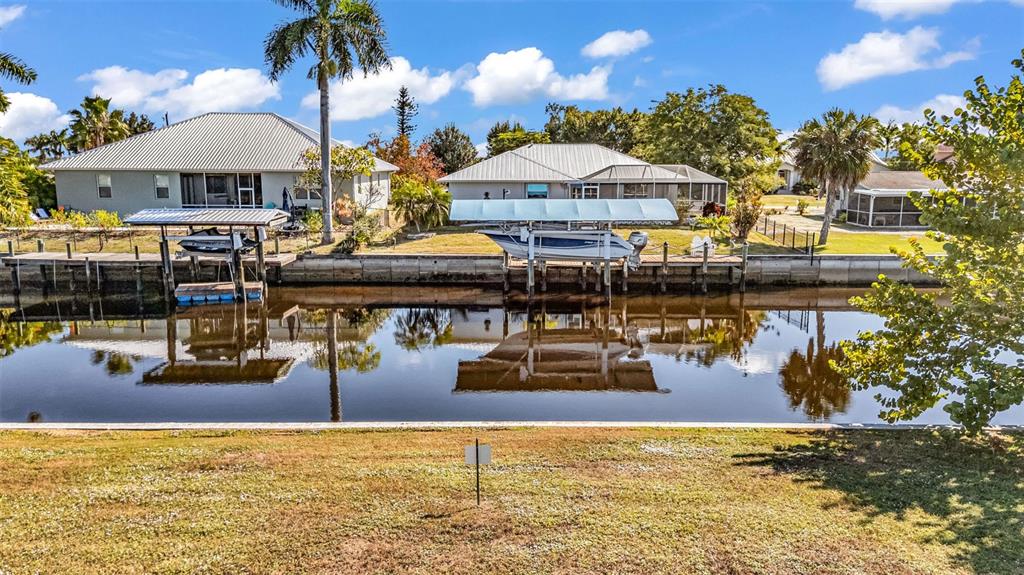 A canal-front view showing two houses with boat lifts and docks under a blue sky — 3334 DOVER DRIVE, PUNTA GORDA, FL