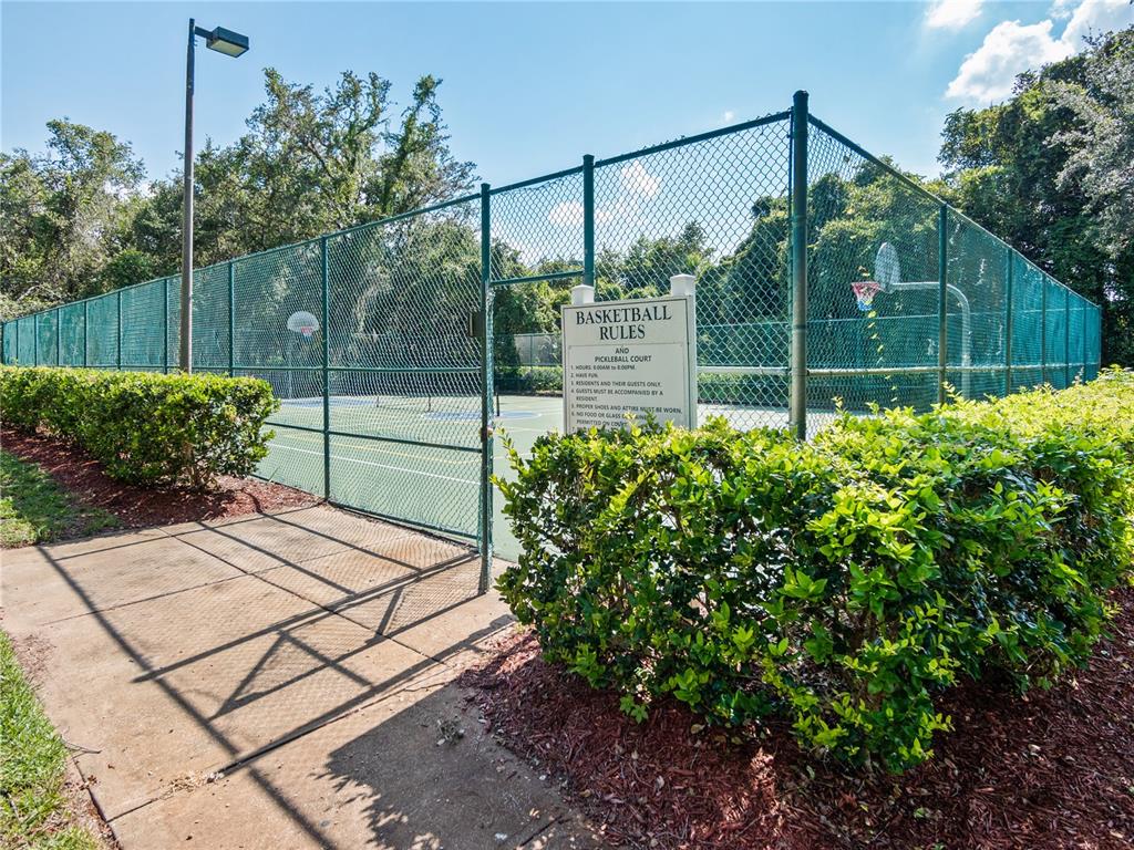 A fenced outdoor basketball and pickleball court is surrounded by green bushes and trees — 8904 LEGACY COURT UNIT 110, KISSIMMEE, FL