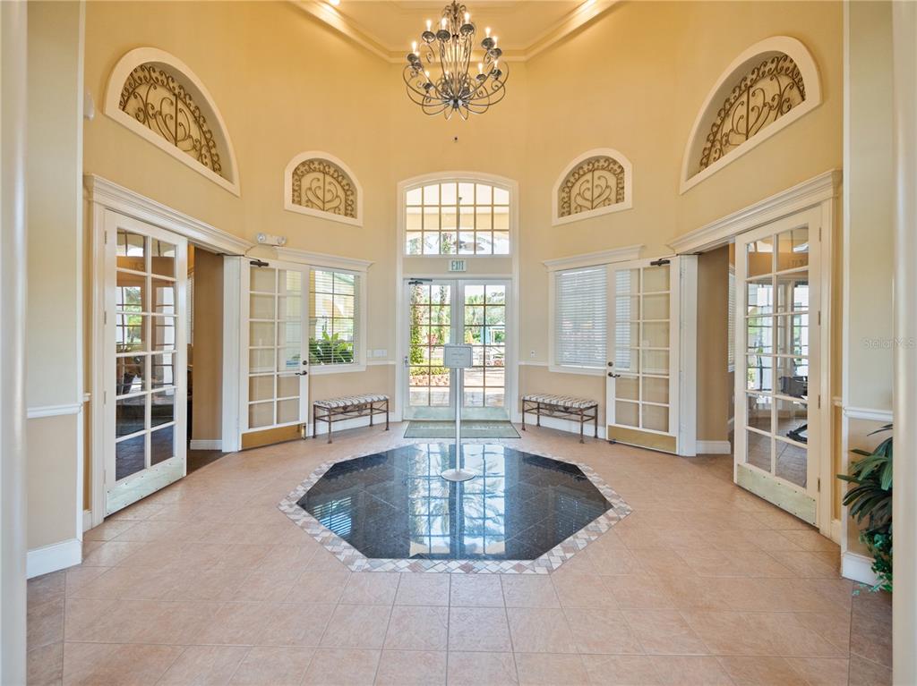 A high-ceilinged lobby features a central octagonal dark tile inlay, chandelier, and multiple glass doors — 8904 LEGACY COURT UNIT 110, KISSIMMEE, FL