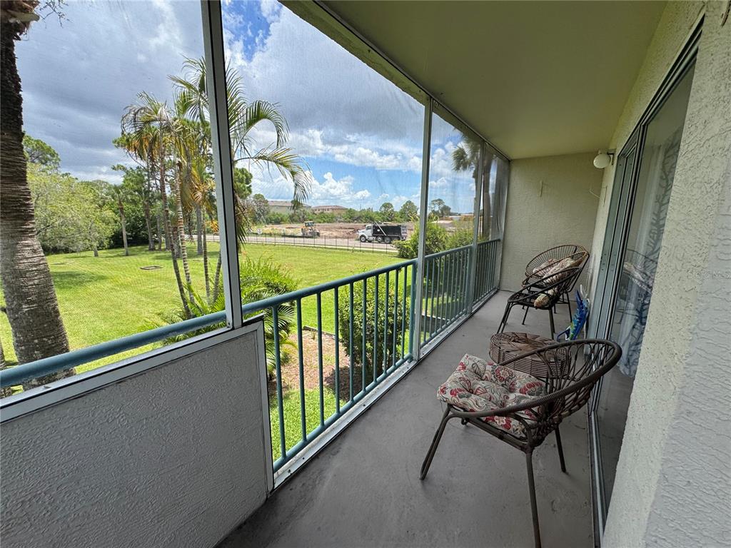 A screened-in balcony features two wicker chairs and overlooks a grassy field and construction site — 5557 SEA FOREST DRIVE UNIT 118, NEW PORT RICHEY, FL
