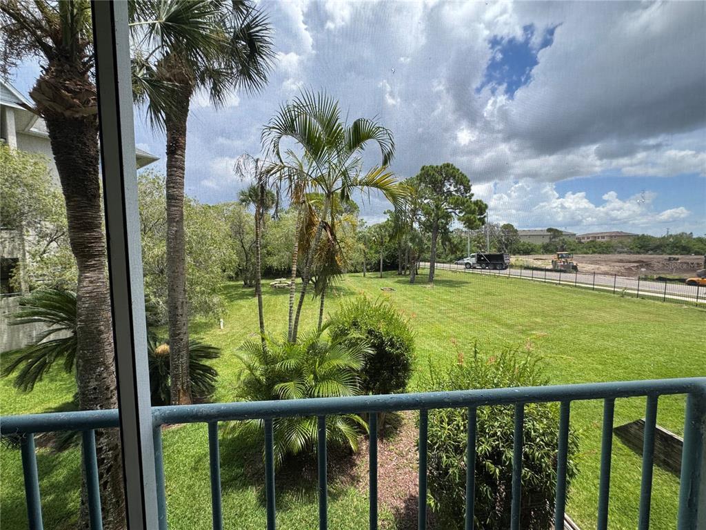 A view from a screened balcony overlooking a grassy yard with palm trees and construction — 5557 SEA FOREST DRIVE UNIT 118, NEW PORT RICHEY, FL