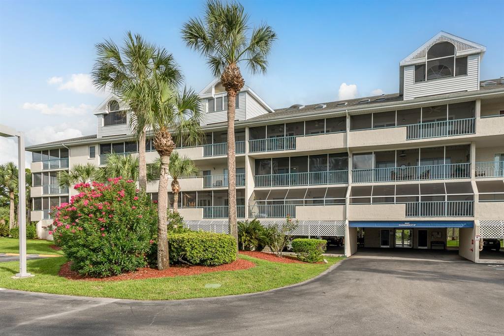 A multi-story apartment building with screened balconies, palm trees, and a ground-level parking area — 5557 SEA FOREST DRIVE UNIT 118, NEW PORT RICHEY, FL