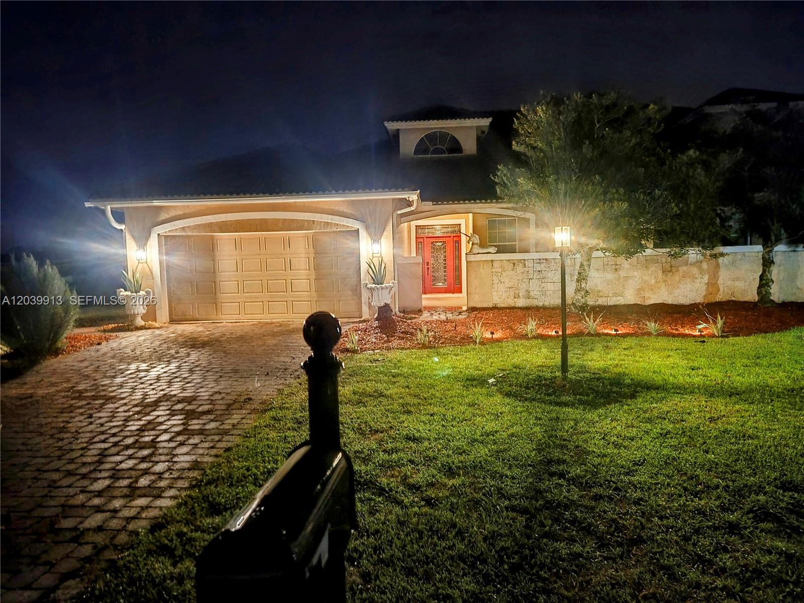 A night view of a house exterior with a paved driveway, garage, and front entrance — 6938 Cecilia Ave, Sebring FL 33872, SEBRING, FL