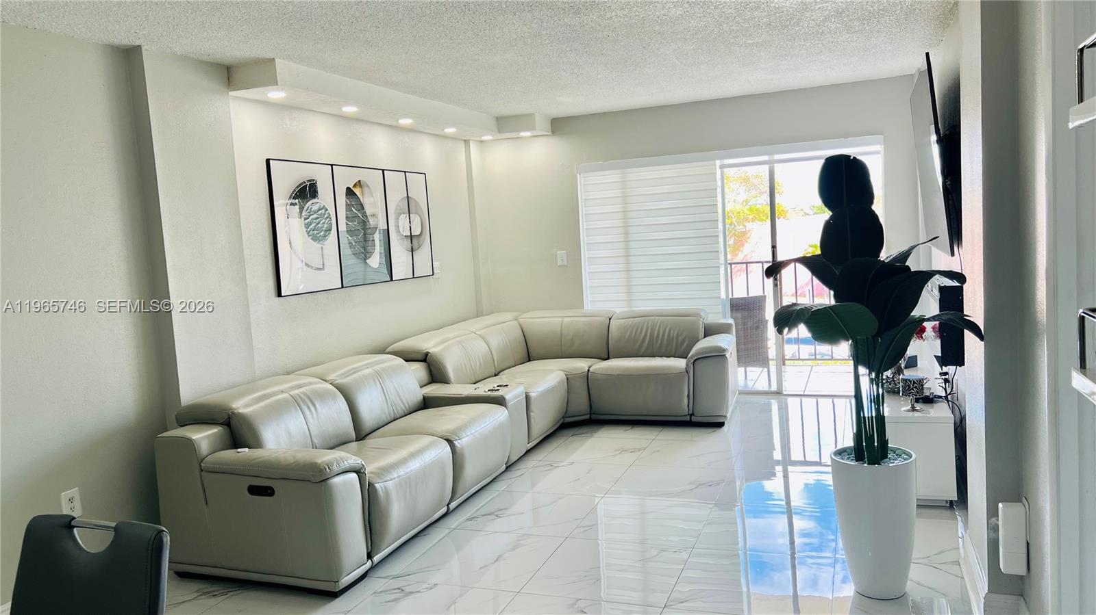 A living room features a large light-colored sectional sofa, marble-look tile floors, and recessed lighting — 14250 SW 62nd St # 319, Miami FL 33183, MIAMI, FL