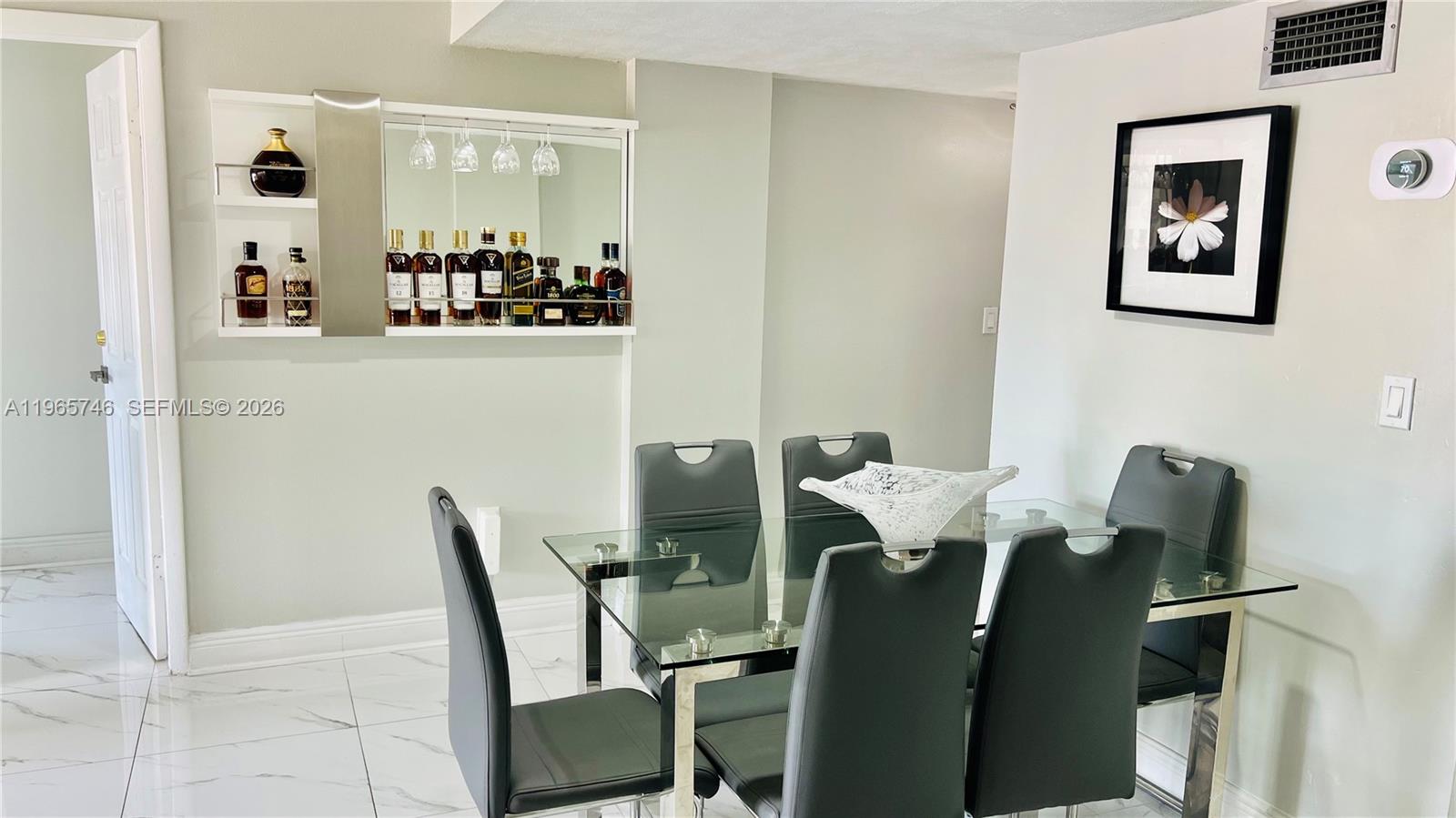 A dining room features a glass table, black chairs, and a wall-mounted mirrored bar — 14250 SW 62nd St # 319, Miami FL 33183, MIAMI, FL