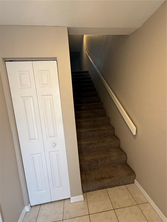 A carpeted staircase leads upward next to a white bifold closet door on tiled flooring — 1117 PINELLAS BAYWAY S UNIT 303, TIERRA VERDE, FL