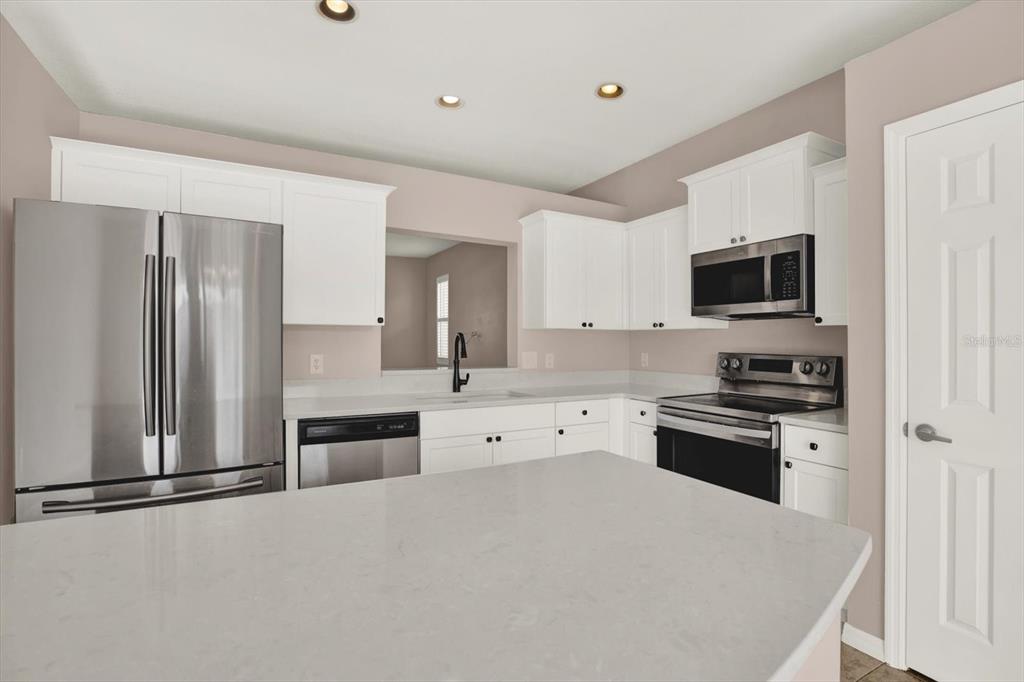 A kitchen features white cabinets, stainless steel appliances, and a light-colored quartz island countertop — 14316 HOLLY HAMMOCK LANE, BROOKSVILLE, FL