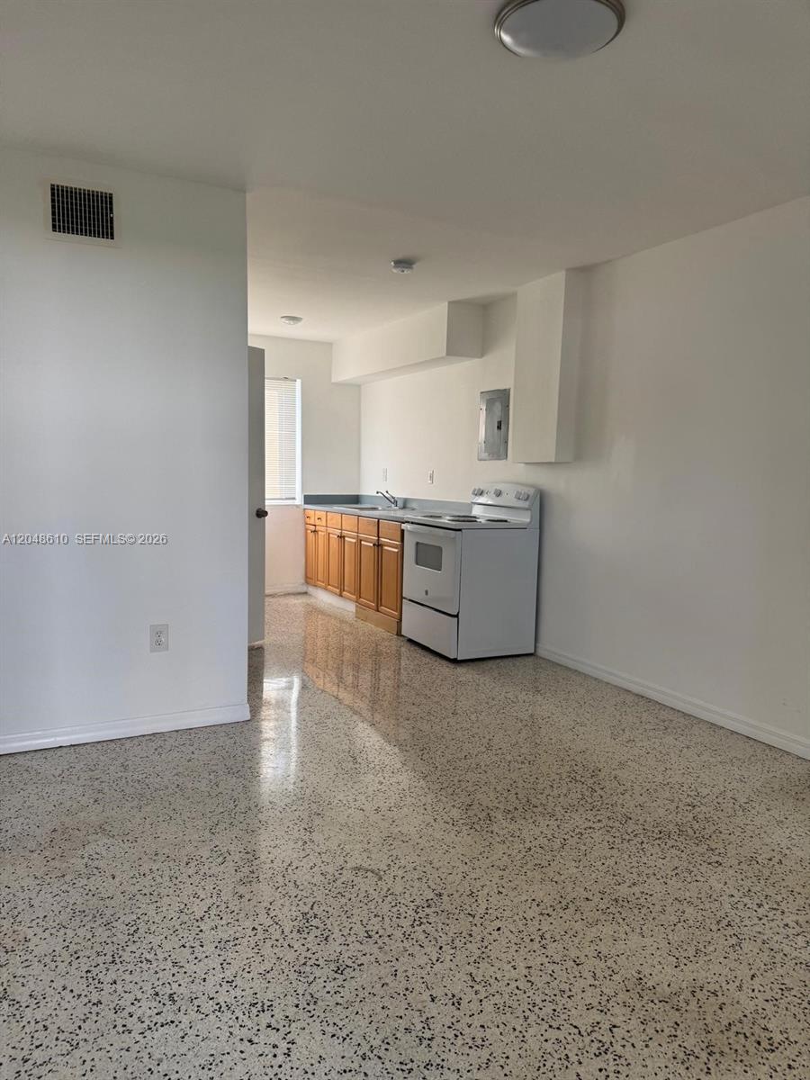 A kitchen with wooden cabinets, a white stove, and speckled flooring in an open room — 680 NE 88th Ter # 2, Miami FL 33138, MIAMI, FL