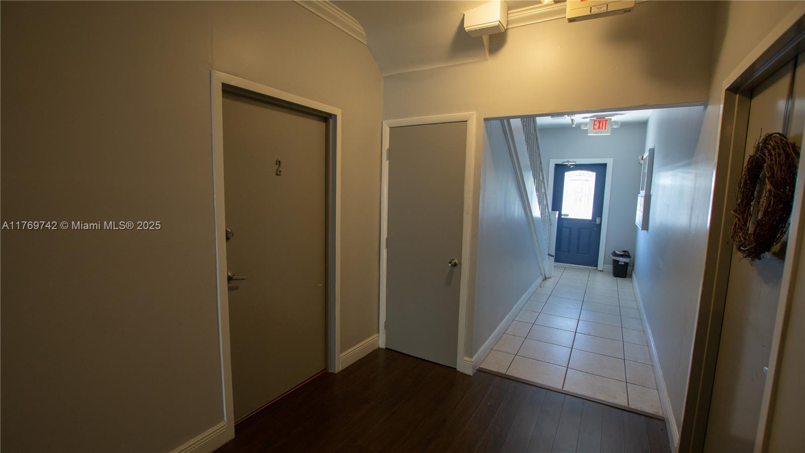An indoor hallway features two gray doors, dark wood flooring, and a tiled exit path — 577 NE 62 STREET # 2, Miami FL 33138, MIAMI, FL