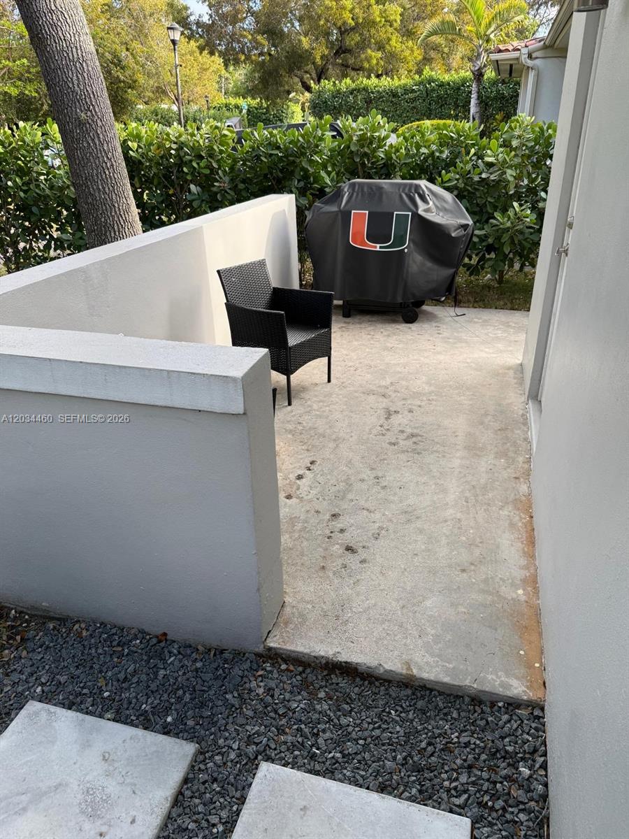 A concrete patio features a black wicker chair and a covered grill near a wall — 400 Miller Rd, Coral Gables FL 33146, CORAL GABLES, FL