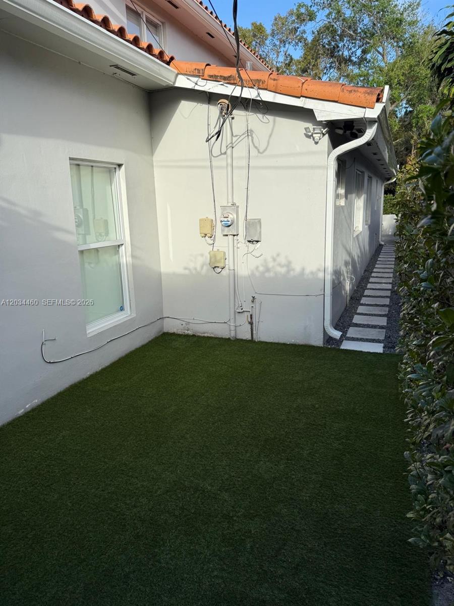 A side view of a house exterior featuring artificial turf, a window, and utility boxes — 400 Miller Rd, Coral Gables FL 33146, CORAL GABLES, FL