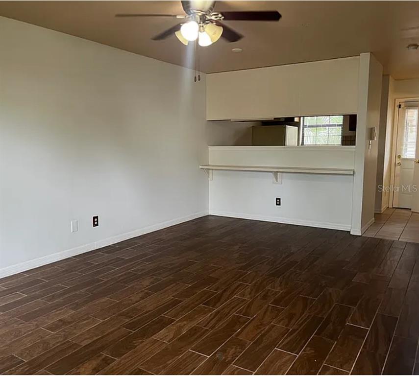 A living room with dark wood-look tile flooring, white walls, and a breakfast bar opening — 2302 MAKI ROAD UNIT 98, PLANT CITY, FL