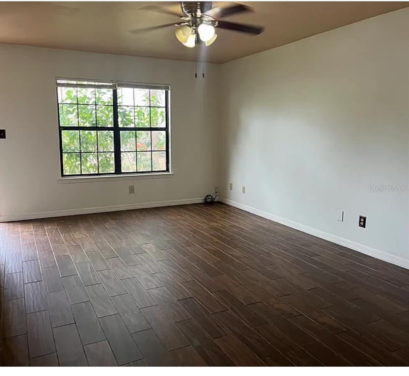 An empty room features dark wood-look tile flooring, white walls, and a ceiling fan — 2302 MAKI ROAD UNIT 98, PLANT CITY, FL