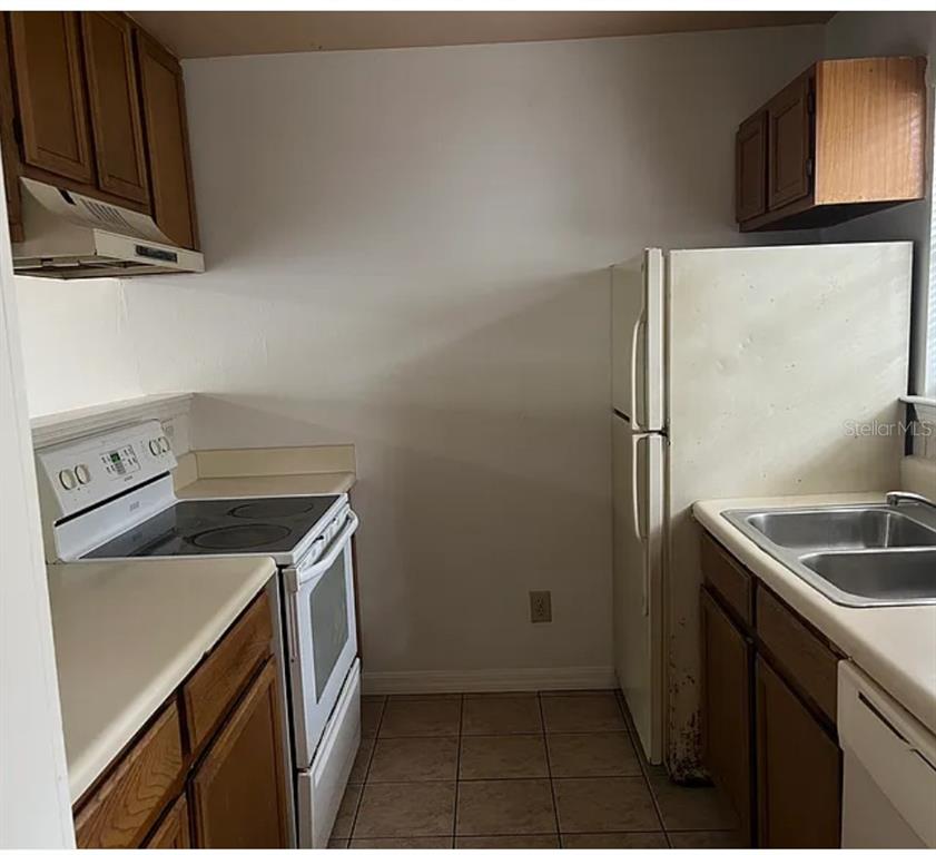 A galley-style kitchen features wood cabinets, white appliances, and light-colored countertops — 2302 MAKI ROAD UNIT 98, PLANT CITY, FL