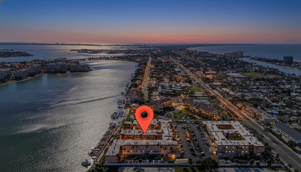 An aerial view shows a waterfront apartment complex at dusk with a red location pin — 8931 BLIND PASS ROAD UNIT 156, ST PETE BEACH, FL