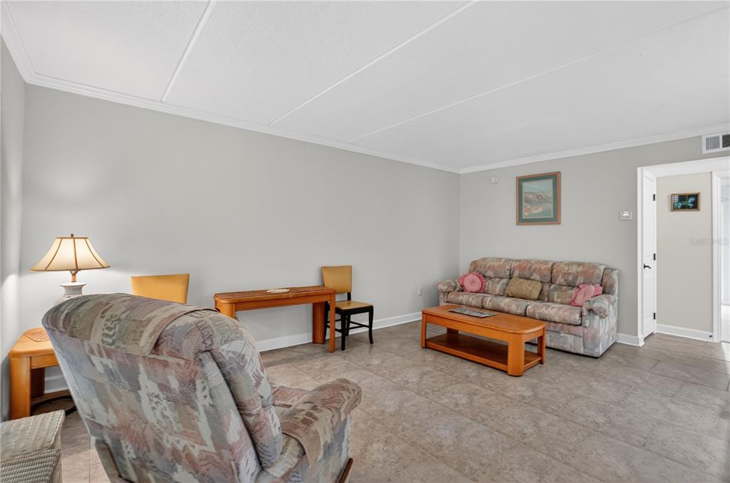 A living room features tile flooring, a patterned sofa, a wooden coffee table, and chairs — 8931 BLIND PASS ROAD UNIT 156, ST PETE BEACH, FL