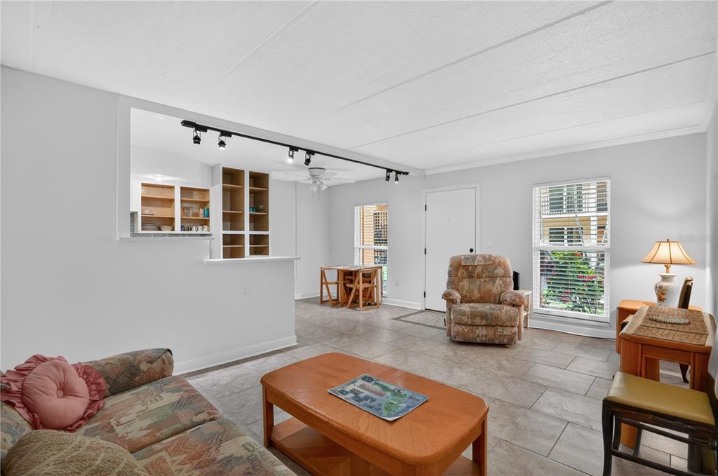 A living room with tile floors, a pass-through kitchen window, and a dining area — 8931 BLIND PASS ROAD UNIT 156, ST PETE BEACH, FL