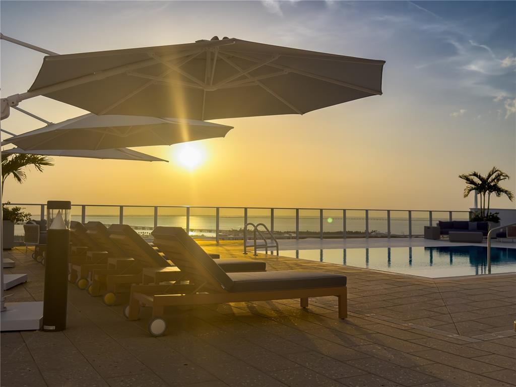 A rooftop pool deck features lounge chairs, umbrellas, and a view of the sunset — 5713 BOWEN DANIEL DRIVE UNIT 703, TAMPA, FL