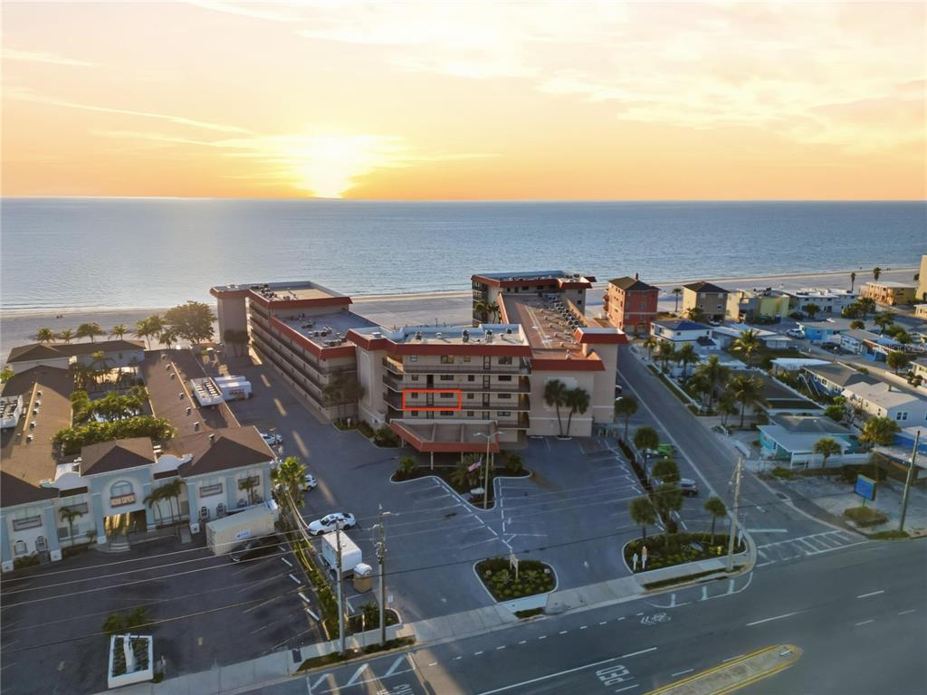 An aerial view shows a multi-story beachfront hotel with a parking lot at sunset — 17580 GULF BOULEVARD UNIT 302, REDINGTON SHORES, FL