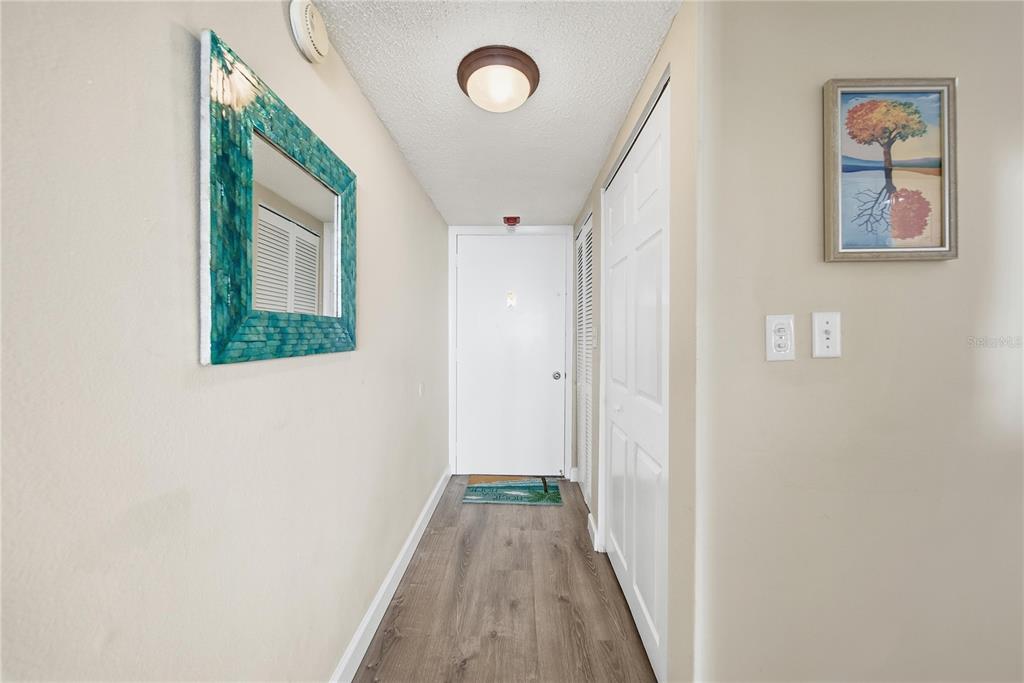 A hallway features wood-look flooring, a blue-framed mirror, and a white entry door — 17580 GULF BOULEVARD UNIT 302, REDINGTON SHORES, FL