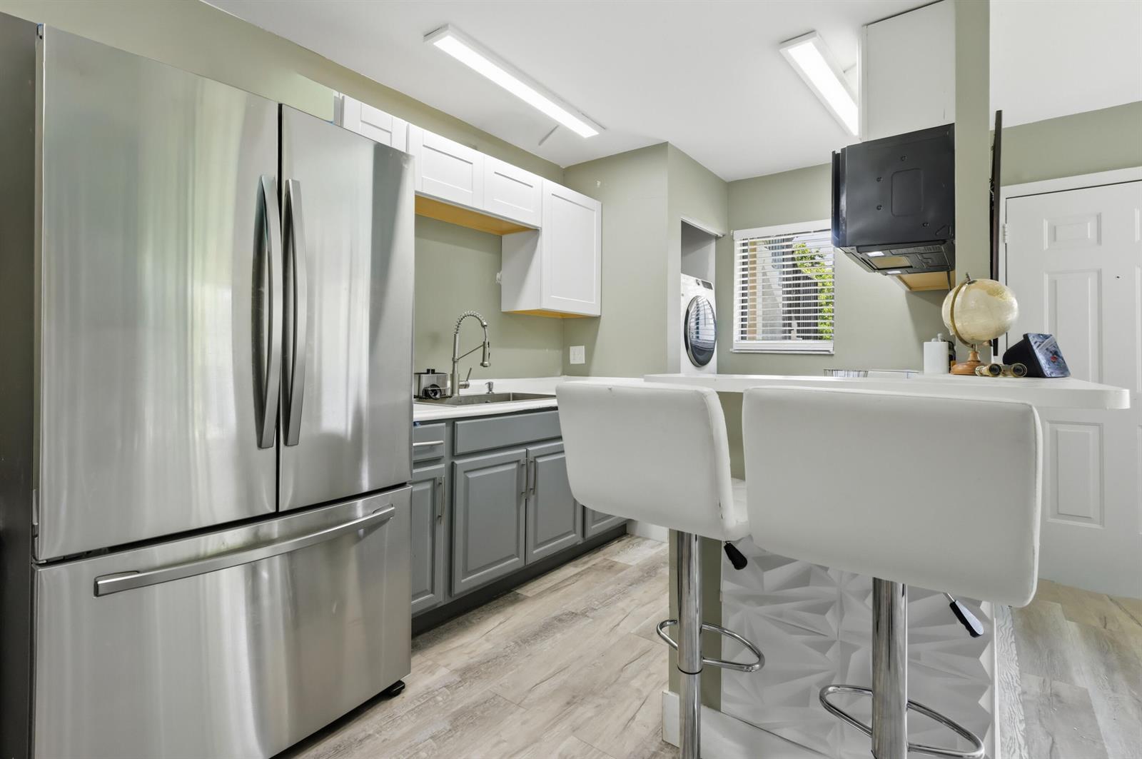 A kitchen features stainless steel appliances, gray lower cabinets, white upper cabinets, and a breakfast bar — 545 Trace Circle # 102, Deerfield Beach FL 33441, DEERFIELD BEACH, FL
