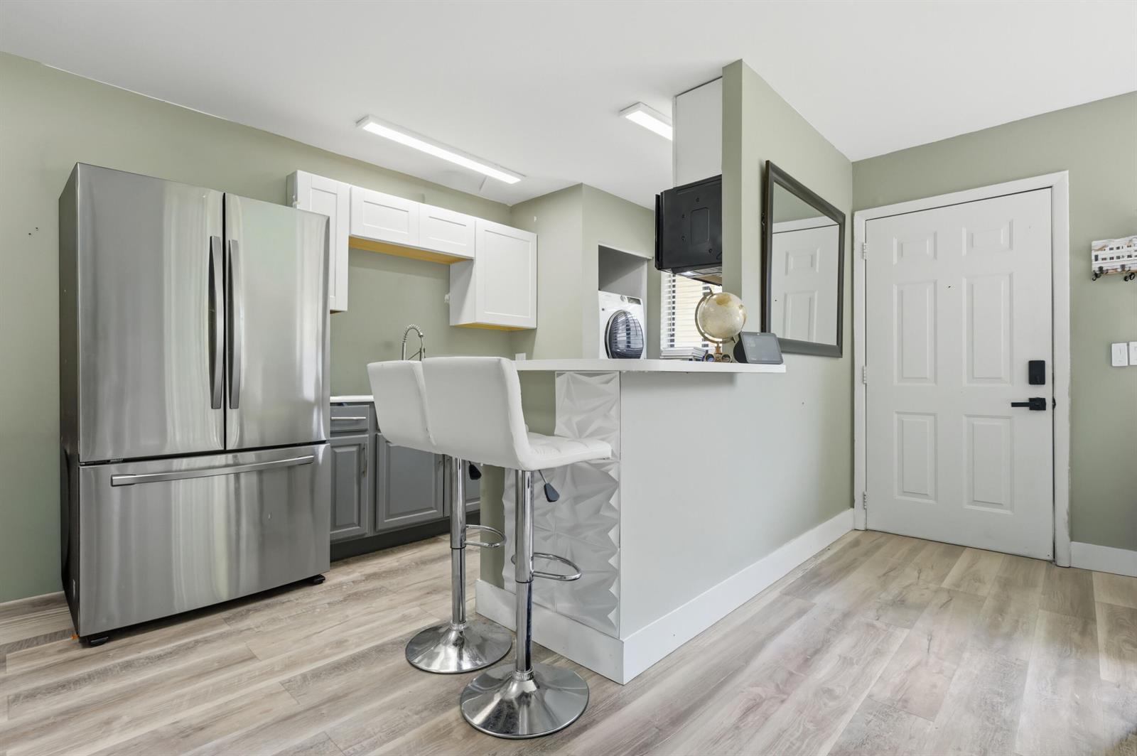 A kitchen features stainless steel appliances, white upper cabinets, gray lower cabinets, and bar seating — 545 Trace Circle # 102, Deerfield Beach FL 33441, DEERFIELD BEACH, FL