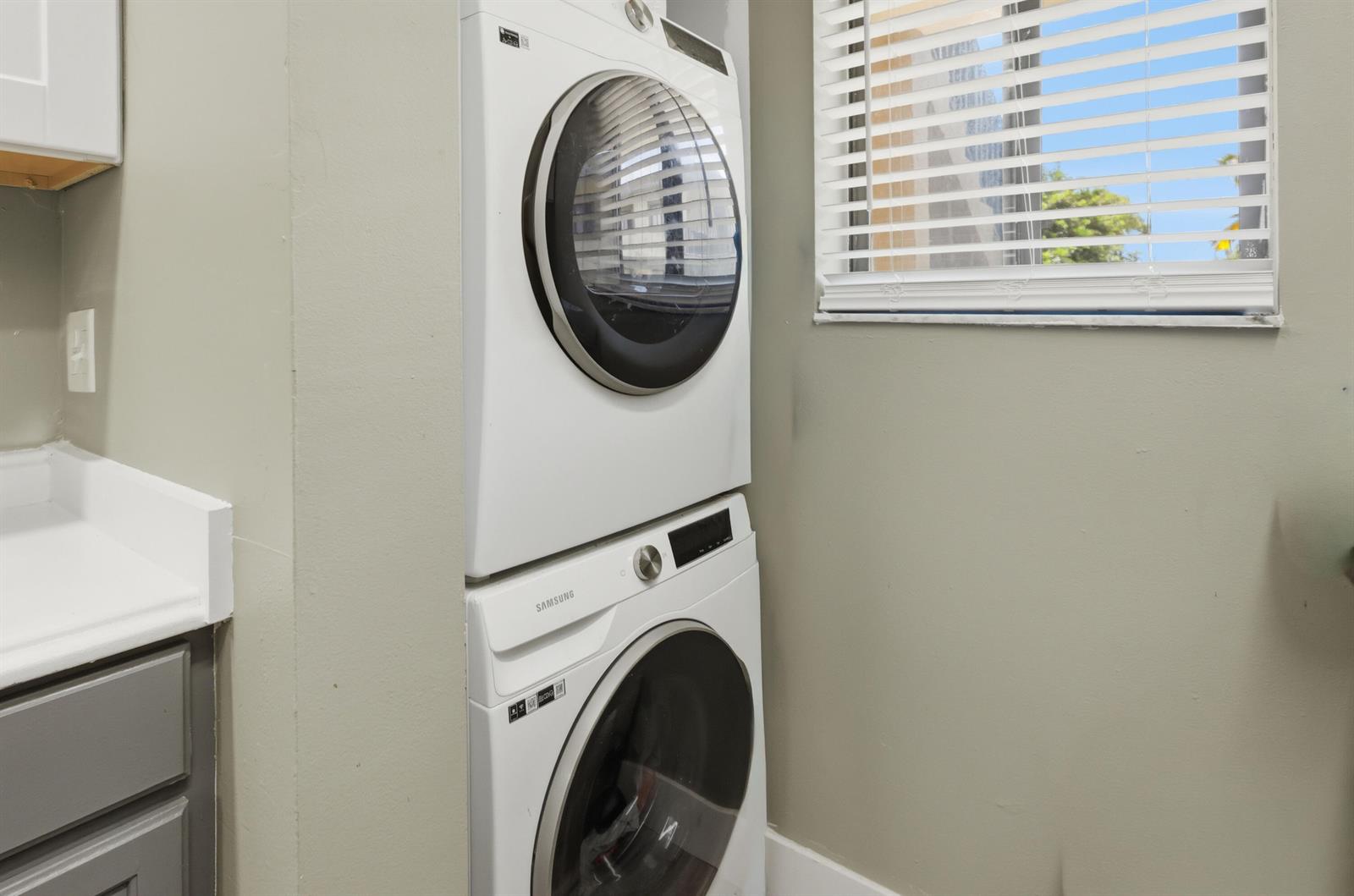 A stacked Samsung washer and dryer unit sits in a laundry room with a window — 545 Trace Circle # 102, Deerfield Beach FL 33441, DEERFIELD BEACH, FL