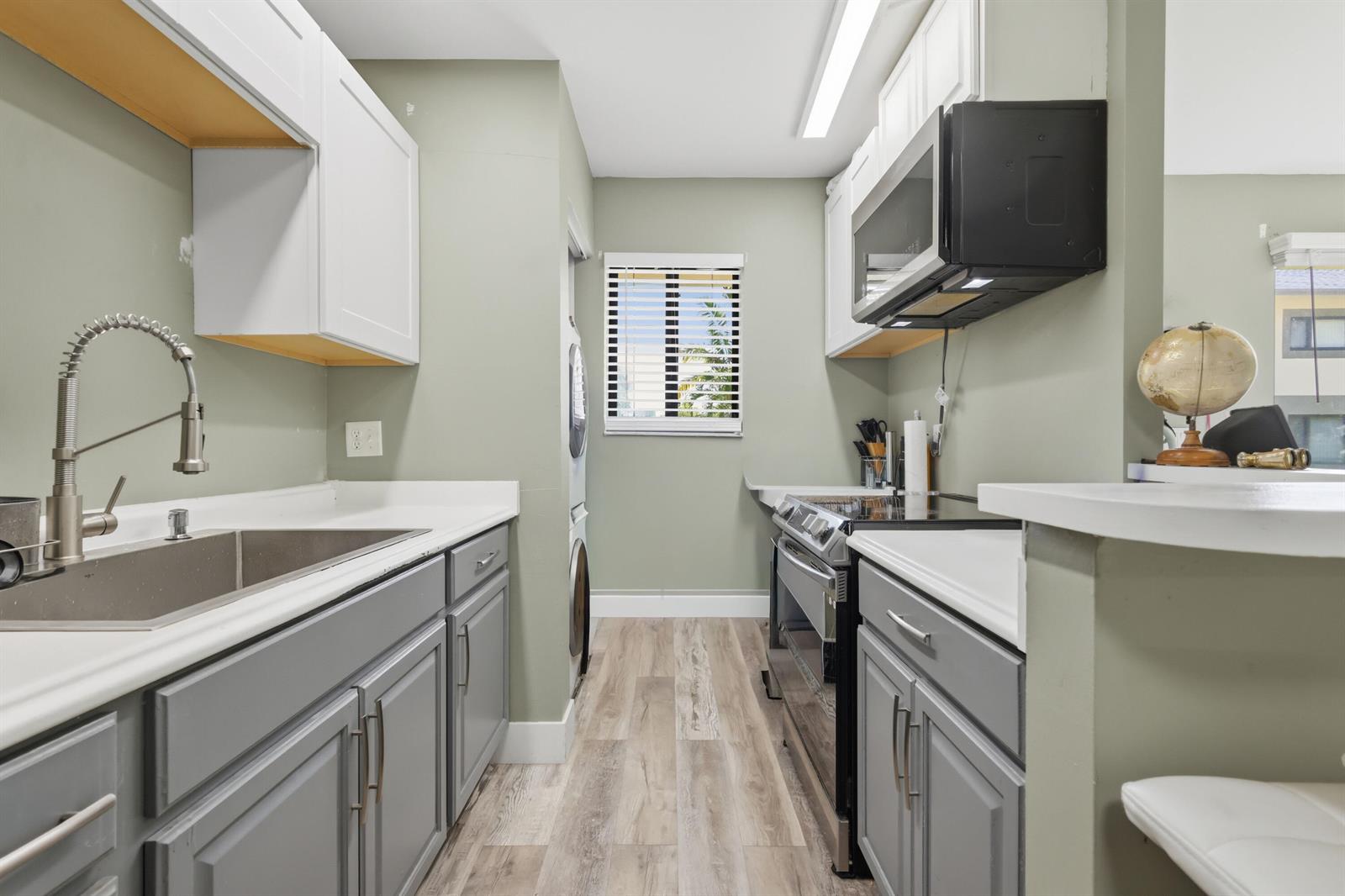 A galley kitchen features gray lower cabinets, white upper cabinets, stainless steel appliances, and wood-look flooring — 545 Trace Circle # 102, Deerfield Beach FL 33441, DEERFIELD BEACH, FL