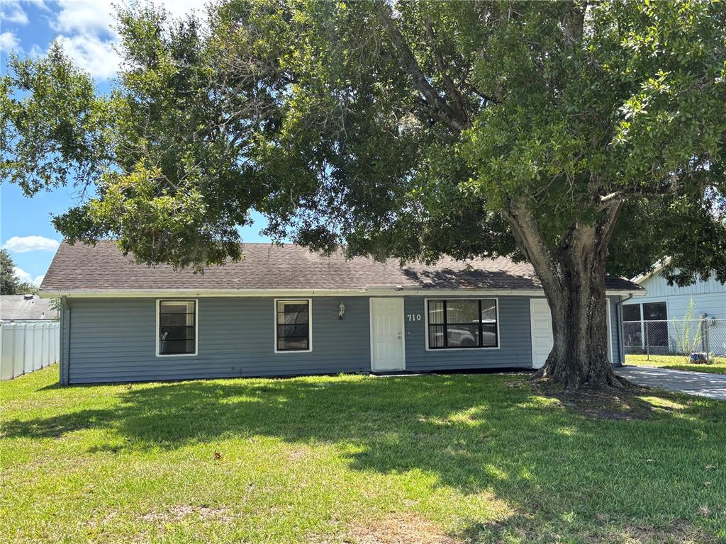 A single-story house with blue siding and a large tree in the front yard — 710 BUNKER LANE, POINCIANA, FL