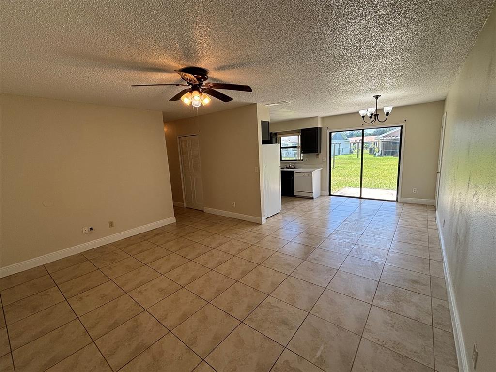 An open-concept living and dining area features beige tile flooring, a ceiling fan, and kitchen — 710 BUNKER LANE, POINCIANA, FL