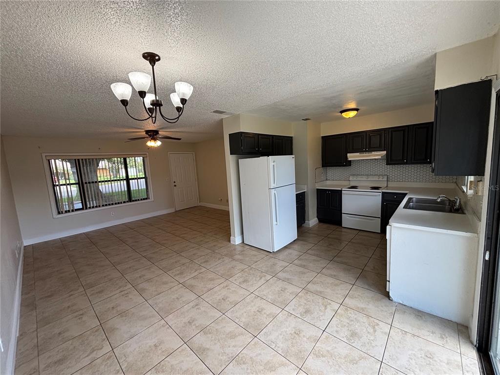 An open-concept kitchen and dining area features tile flooring, dark cabinetry, and white appliances — 710 BUNKER LANE, POINCIANA, FL