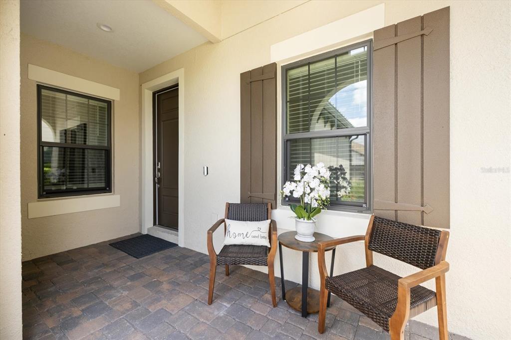 A covered front porch features paver flooring, two chairs, a small table, and a front door — 27540 JANZEN COURT, ENGLEWOOD, FL