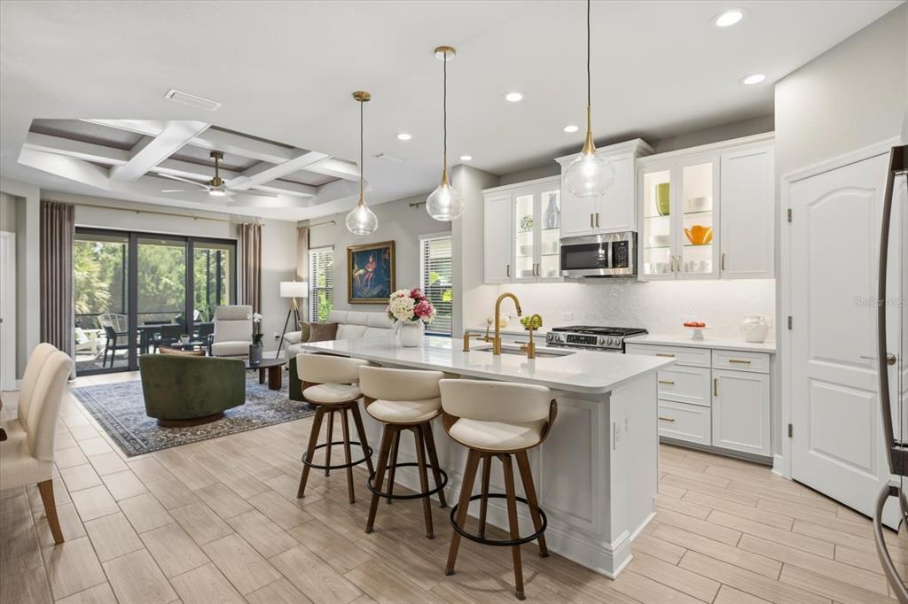 A kitchen with a white island and bar stools opens into a living room area — 27540 JANZEN COURT, ENGLEWOOD, FL