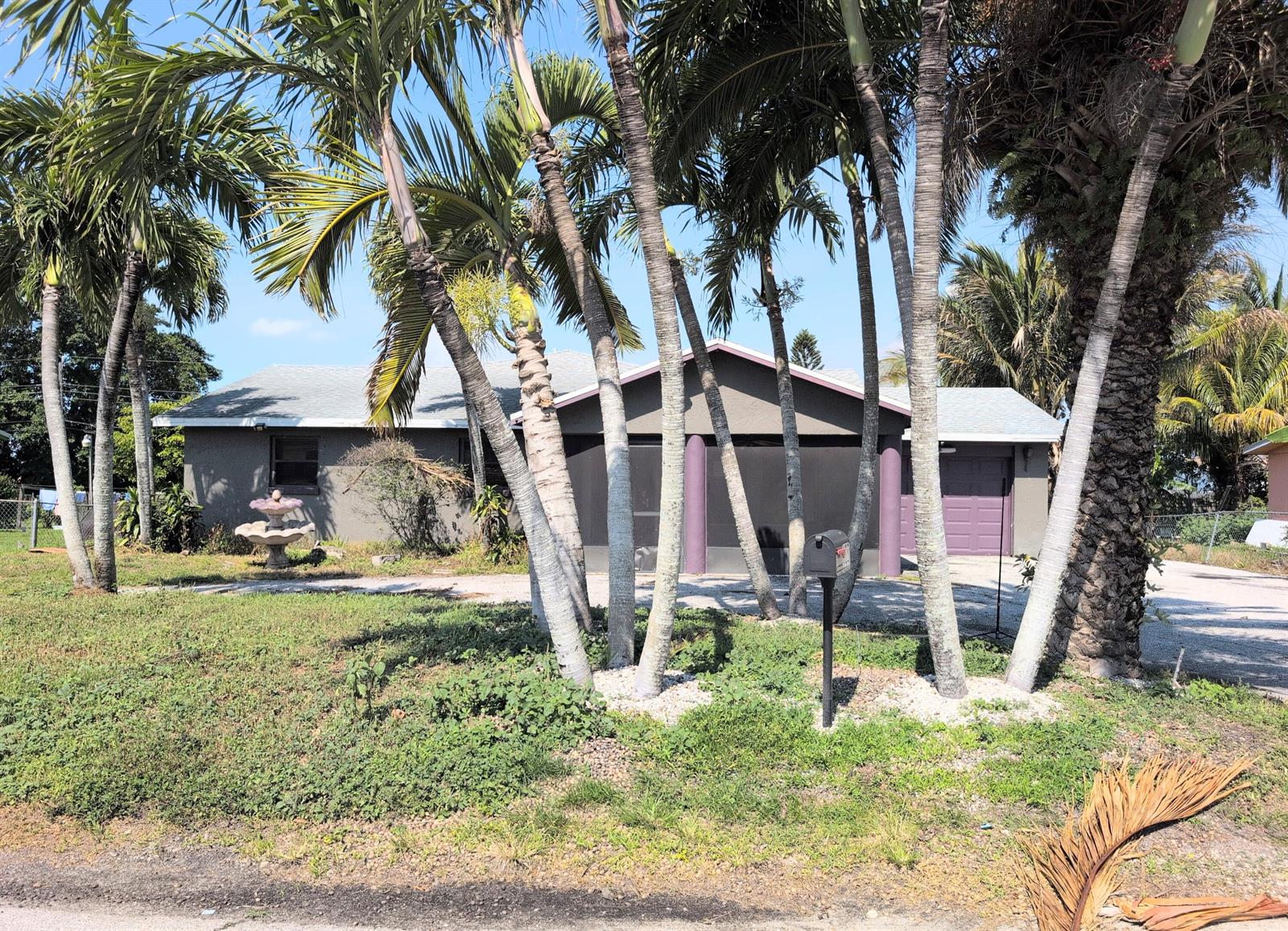 A single-story house with a screened front porch, purple garage door, and several palm trees — 455 Janice Avenue, South Bay FL 33493, SOUTH BAY, FL