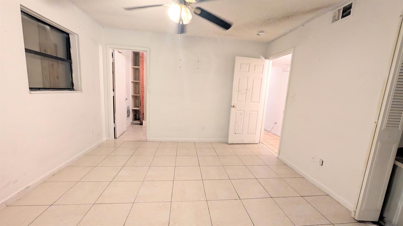 An empty room with white walls, tile flooring, a ceiling fan, and two doorways — 455 Janice Avenue, South Bay FL 33493, SOUTH BAY, FL