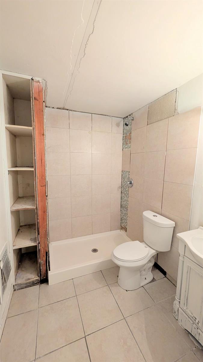 A bathroom features a tiled shower stall, an adjacent open shelving unit, and a toilet — 455 Janice Avenue, South Bay FL 33493, SOUTH BAY, FL