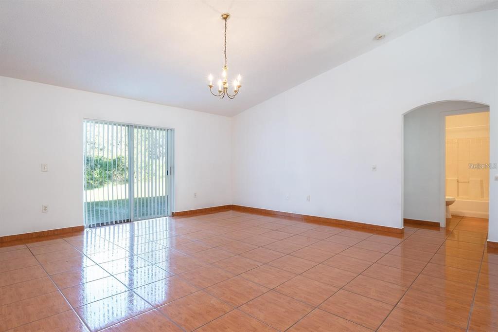 An empty room with tan tile flooring, a vaulted ceiling, and a sliding glass door — 718 PINCON LANE, KISSIMMEE, FL