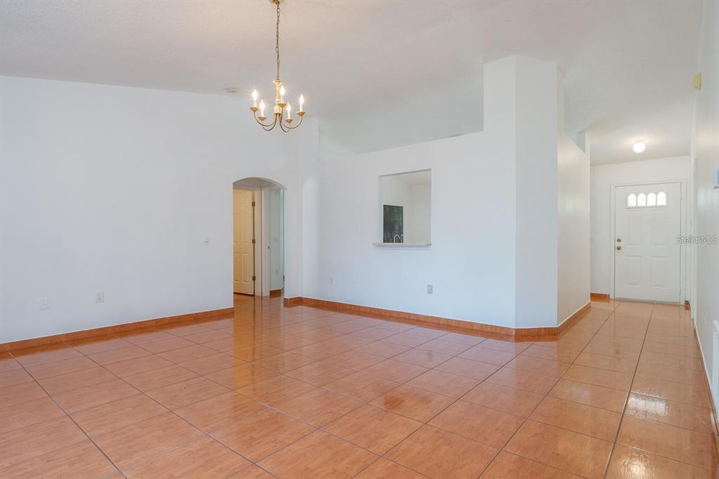 An empty room with tiled floors, a chandelier, and a pass-through window to the kitchen — 718 PINCON LANE, KISSIMMEE, FL